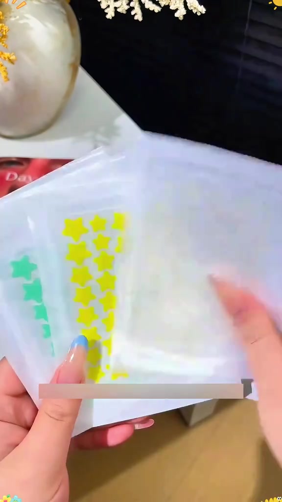 มือถือแผ่นฟิล์มบรรจุแผ่นแปะสิวรูปดาวสีเหลืองและสีเขียวเรียงเป็นแถวหลายดวง