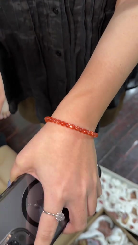 กำไลหินเม็ดเล็กสีแดงสวมบนข้อมือเรียว เห็นขนาดเม็ดที่เล็กเรียบเนียน