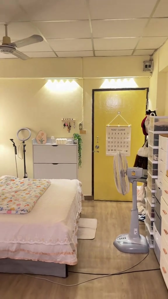 ห้องเช่าหลังปูเสื่อน้ำมันลายไม้ ดูอบอุ่นขึ้น มีเตียง ผ้าห่มพับ พัดลมตั้งพื้น และประตูสีเหลือง