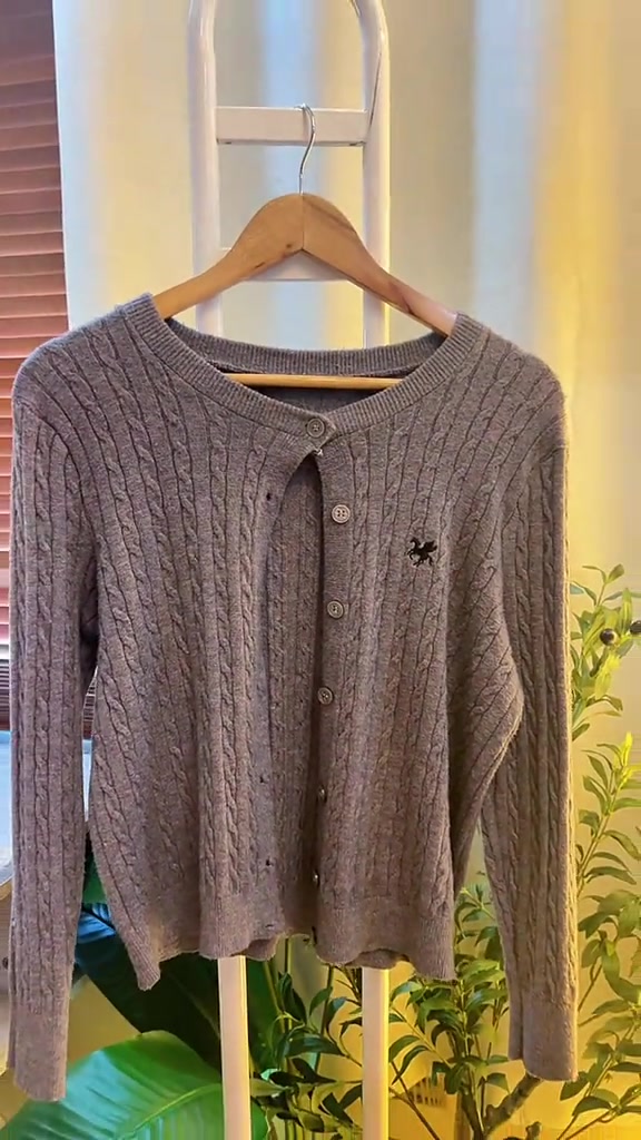 เสื้อคาร์ดิแกนไหมพรมสีเทาอมน้ำตาลลายถักเปียแขวนบนไม้แขวนเสื้อเห็นทรงเต็มตัว