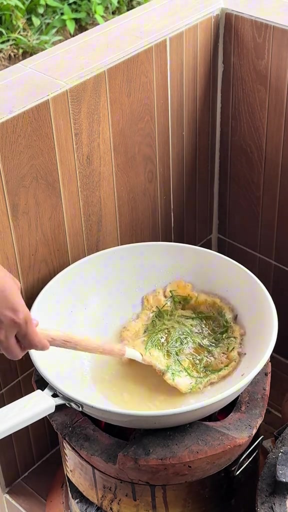 ทอดไข่เจียวใส่ผักในกระทะเคลือบหินอ่อนบนเตา ใช้ตะหลิวช้อนขอบไข่