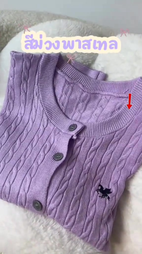 เสื้อคาร์ดิแกนไหมพรมสีม่วงพาสเทลลายถักเปียพับวางบนพื้นขนสีขาว