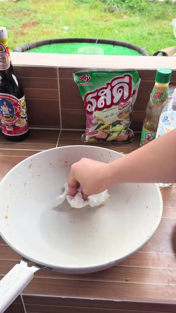 มือใช้กระดาษทิชชูเช็ดด้านในกระทะเคลือบหินอ่อนบนเคาน์เตอร์ครัว