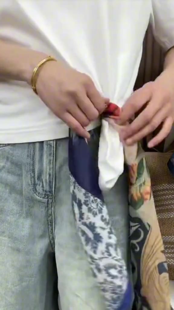 มือกำลังผูกปมผ้าพันคอที่ด้านหน้าเอวกางเกงยีนส์สีอ่อน