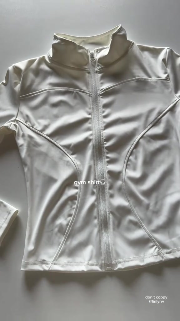 เสื้อออกกำลังกายแขนยาวซิปหน้าวางราบอีกมุมเห็นปกตั้งและผิวผ้าเรียบมัน