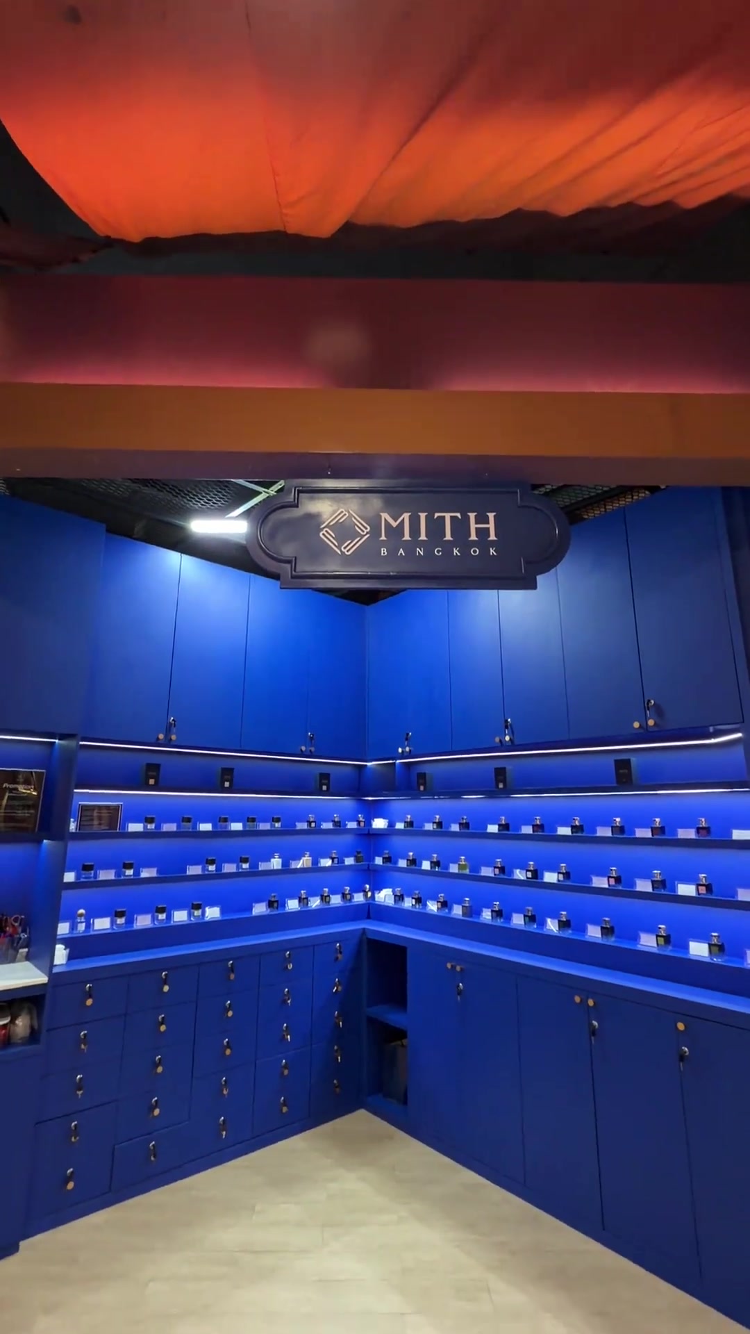 เคาน์เตอร์ MITH Bangkok ผนังและชั้นสีน้ำเงินเรียงขวดน้ำหอมเต็มชั้น พร้อมป้ายโลโก้ MITH Bangkok