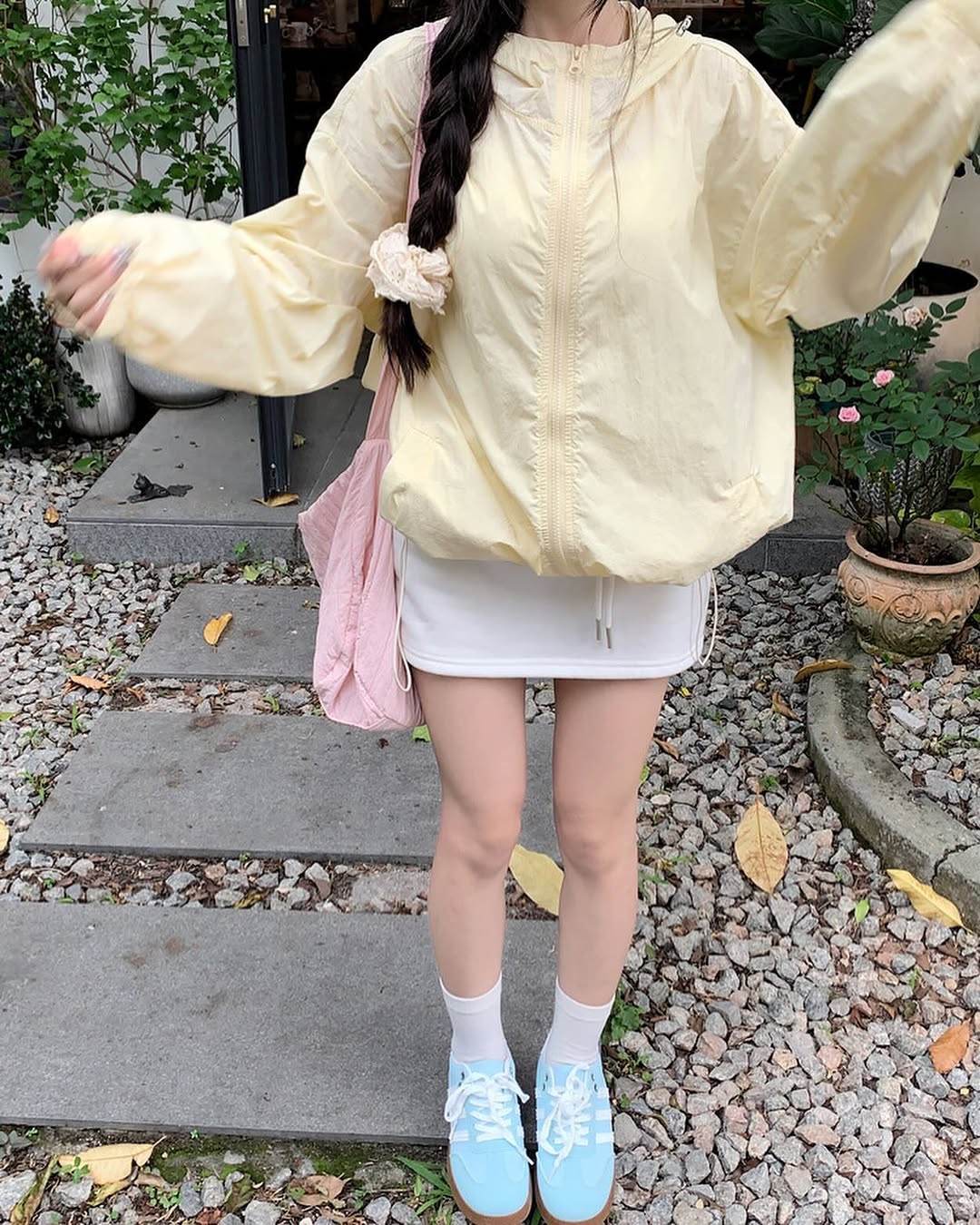 คนสวมเสื้อกันแดดมีฮู้ดทรงหลวมสีเหลืองอ่อนตั้งแต่คอลงมายืนบนทางกรวดกลางแจ้ง