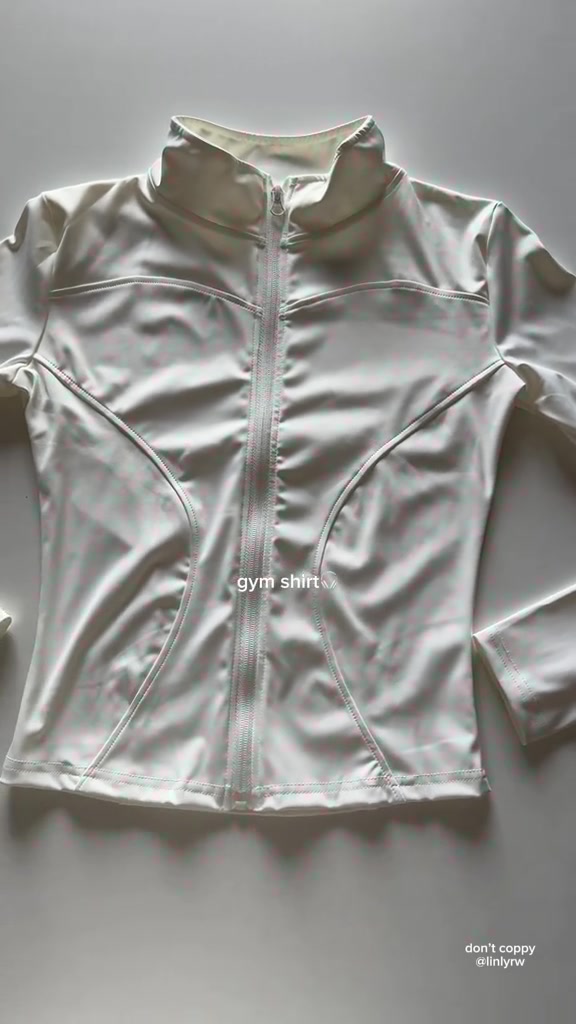 เสื้อออกกำลังกายแขนยาวซิปหน้าสีครีมวางราบเต็มตัวเห็นปกตั้งและซิปปิดจรดคอ