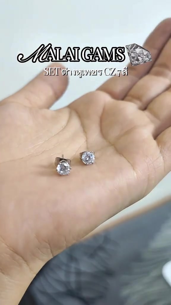 ฝ่ามือวางต่างหูเพชรซีแซดเม็ดขาวหนึ่งคู่ เห็นทั้งหน้าเพชรและก้านกับแป้นด้านหลัง