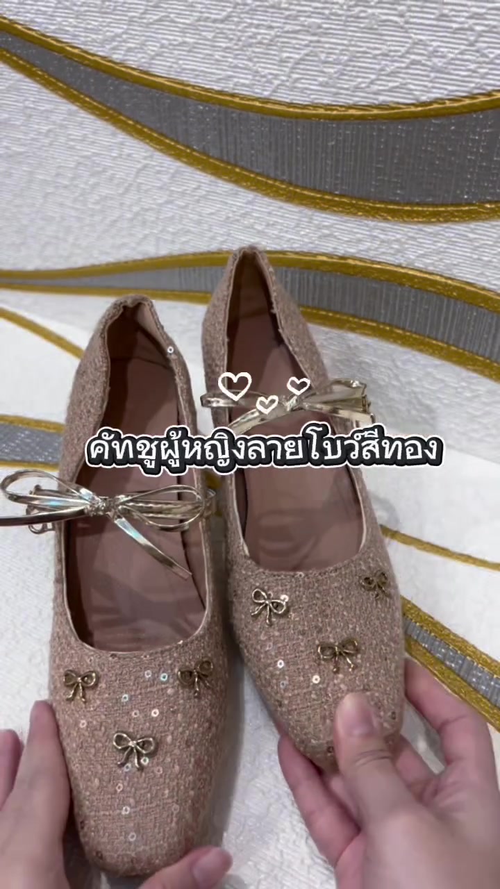 มือประคองรองเท้าคัทชูผ้าถักสีทองอ่อนติดเลื่อมแต่งโบว์โลหะหนึ่งคู่ วางบนผ้าลายคลื่นสีเทาทอง