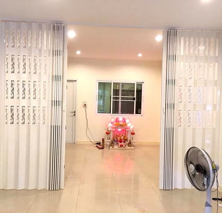 ฉากพับพีวีซีสีขาวถูกพับเก็บไว้คนละฝั่งของช่องกว้างในบ้านจริง มองเห็นห้องโล่งด้านในพร้อมพัดลมตั้งพื้น