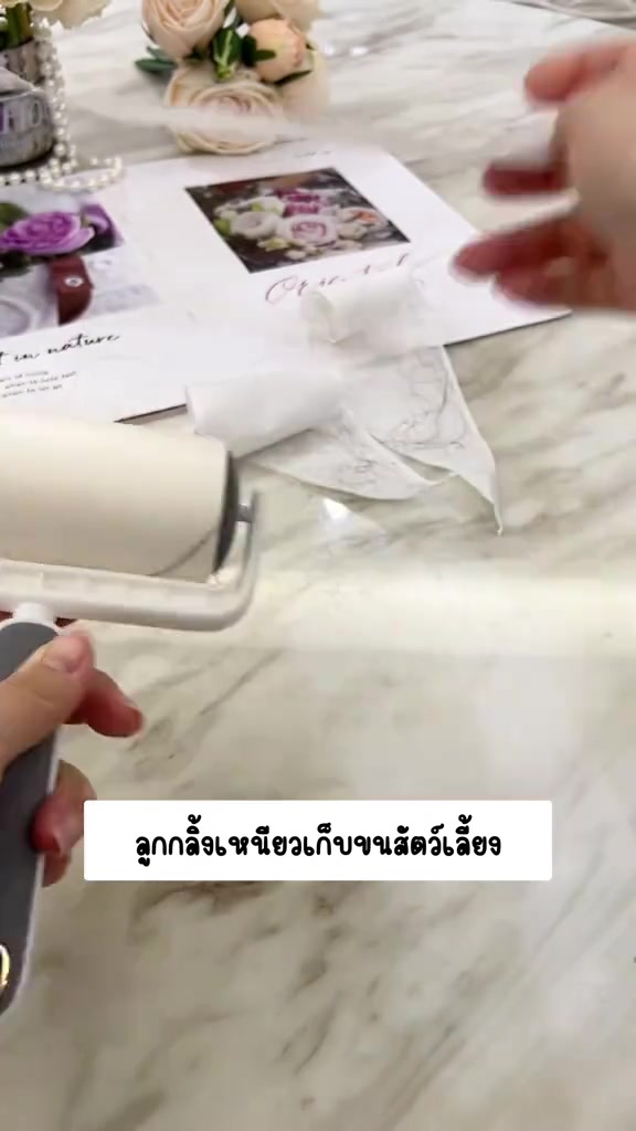ลูกกลิ้งเทปกาวสีขาววางบนโต๊ะลายหินอ่อนพร้อมแผ่นกาวที่ลอกออกมา