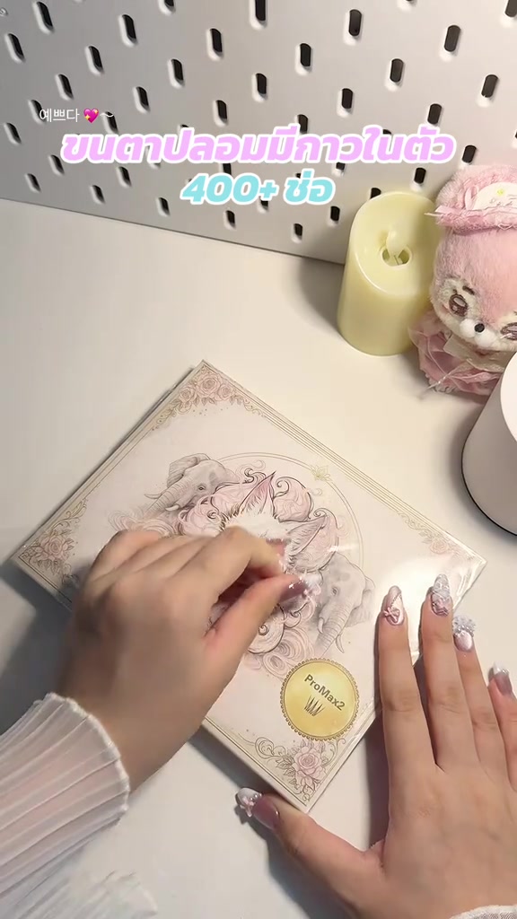 มือกำลังลอกฟิล์มเปิดกล่องขนตาปลอมแบบช่อมีกาวในตัวบนโต๊ะสีขาว
