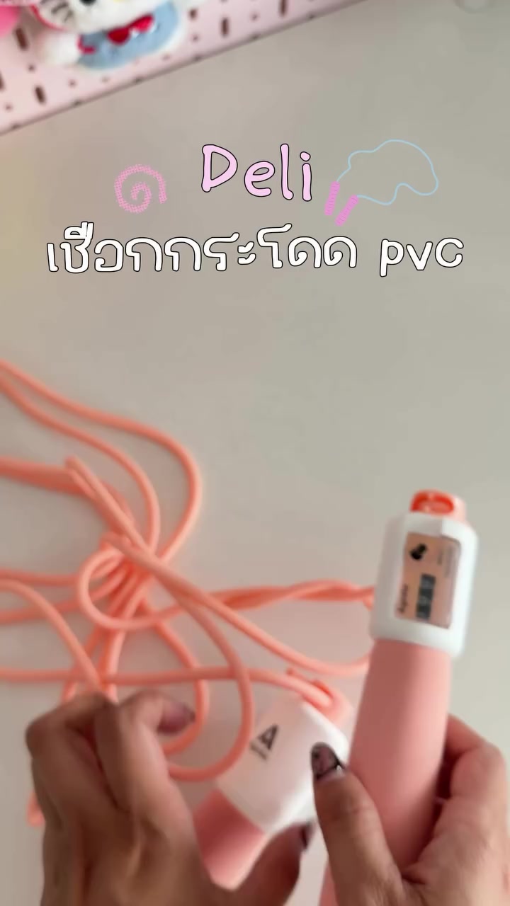 ด้ามเชือกกระโดดสีชมพูขาววางตั้งบนโต๊ะสีขาวข้างสายพีวีซีสีส้มที่ขดเป็นวง