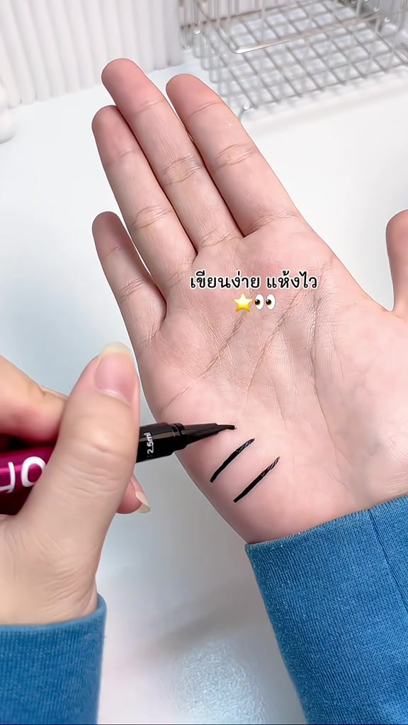 ปลายปากกาอายไลเนอร์กำลังลากเส้นสีดำคมหลายเส้นบนฝ่ามือ