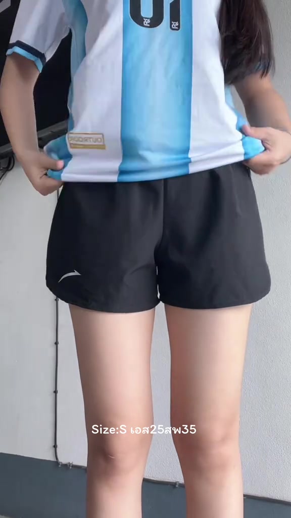 ด้านหน้าของผู้หญิงตั้งแต่คอลงมาใส่กางเกงวิ่งขาสั้นทรงหลวมสีดำ เห็นชายผ้าโปร่งและเอวยางยืด