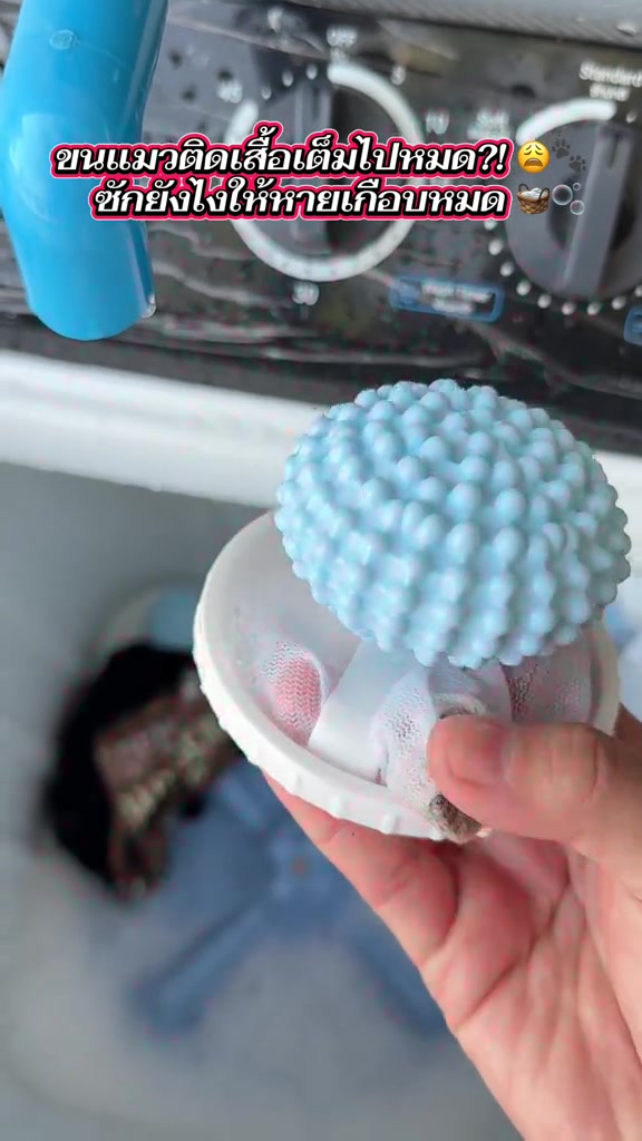 มือถือลูกบอลซักผ้าสีฟ้าผิวปุ่มและถุงตาข่ายสีขาวเหนือถังเครื่องซักผ้า