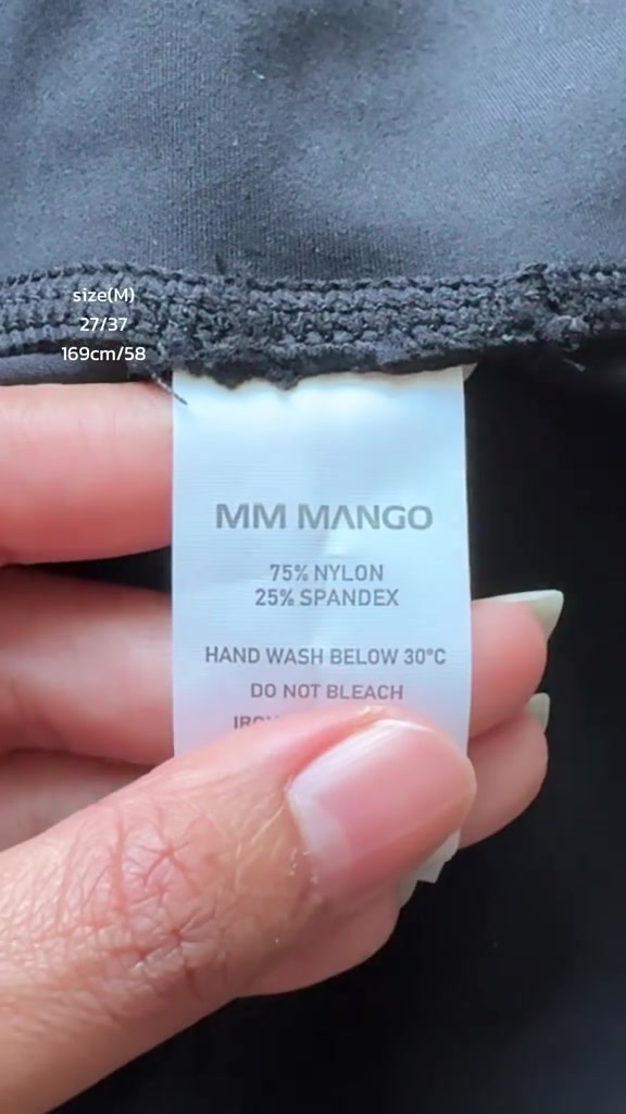 มือถือป้ายเนื้อผ้าด้านในกางเกงออกกำลังกายสีดำ เห็นตัวหนังสือระบุสัดส่วนไนลอนและสแปนเด็กซ์