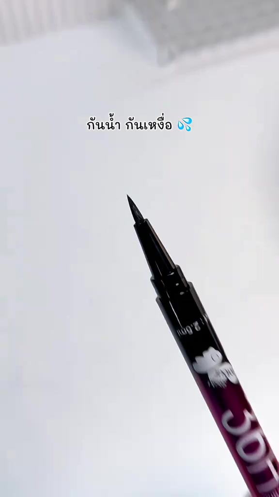 ปลายพู่กันอายไลเนอร์สีดำแหลมเล็กโผล่จากปลอกสีม่วงแดงบนพื้นหลังสีขาว
