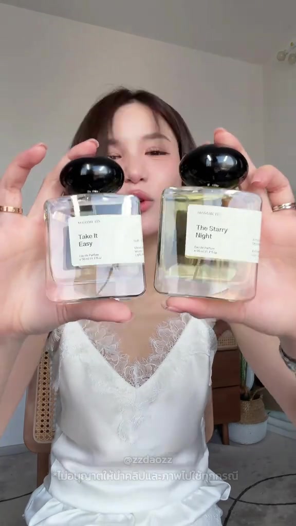 ขวดน้ำหอม Madame Fin x Jenny สองขวดฉลาก Take It Easy และ The Starry Night ฝาดำกลมถูกชูใกล้กล้องจนบังหน้าผู้ถือ