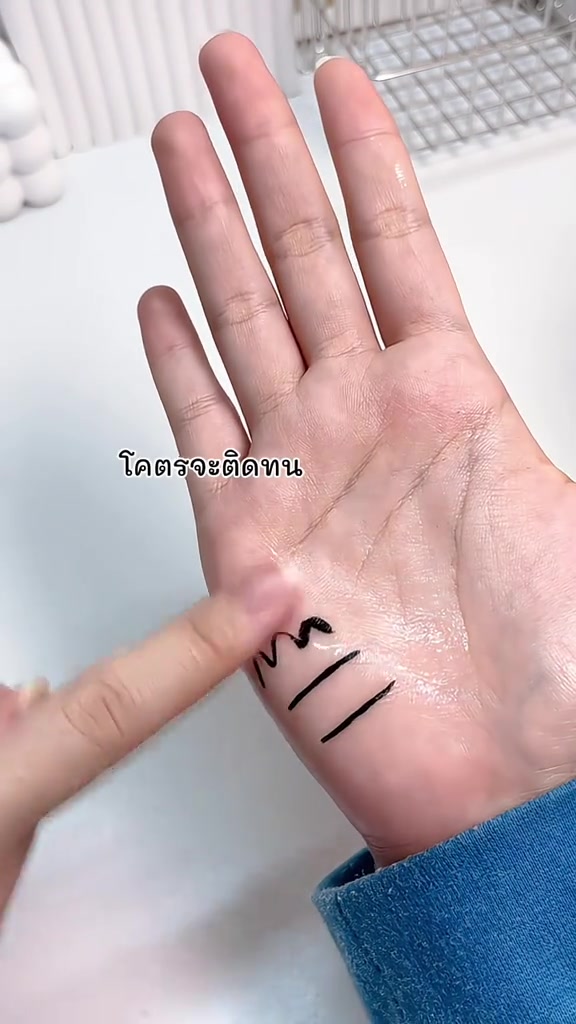 ฝ่ามือที่มีเส้นอายไลเนอร์สีดำหลายเส้นกำลังถูกนิ้วถูขณะผิวเปียกน้ำ แต่เส้นไม่เลือน