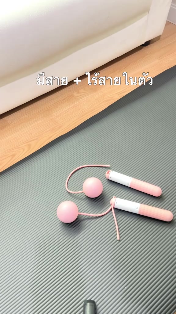 ด้ามเชือกกระโดดสีชมพูขาวสองด้ามวางบนเสื่อโยคะสีเทาพร้อมลูกตุ้มกลมสีชมพูและสายสั้น