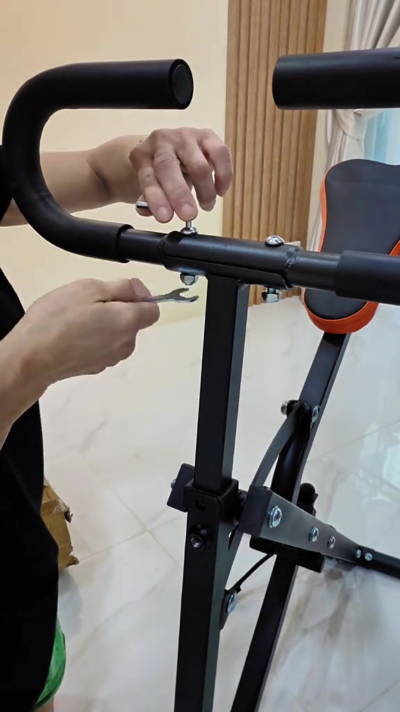 มือสองข้างใช้ประแจขันน็อตยึดที่จับโฟมเข้ากับโครงเหล็กสีดำของม้าโยกออกกำลังกาย