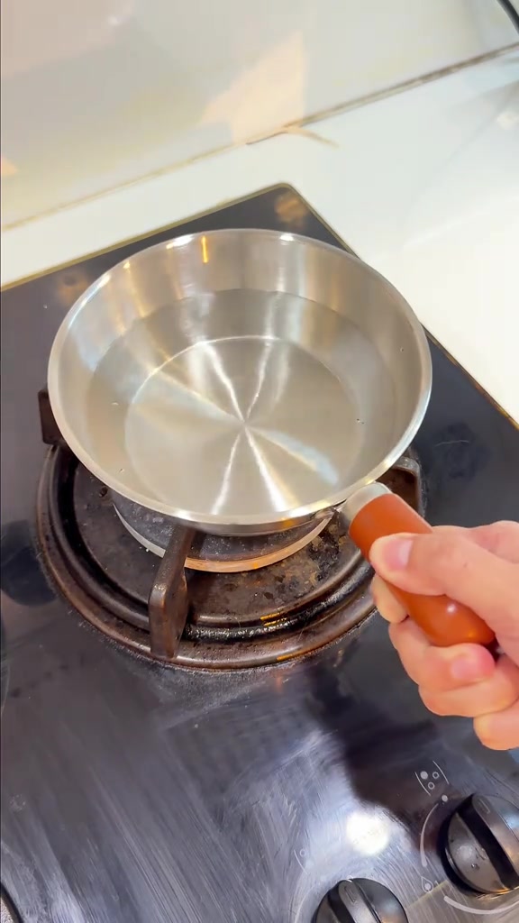 หม้อแสตนเลสด้ามไม้ใส่น้ำวางบนหัวเตาแก๊ส มือจับด้ามไว้ให้เห็นขนาดเทียบมือ