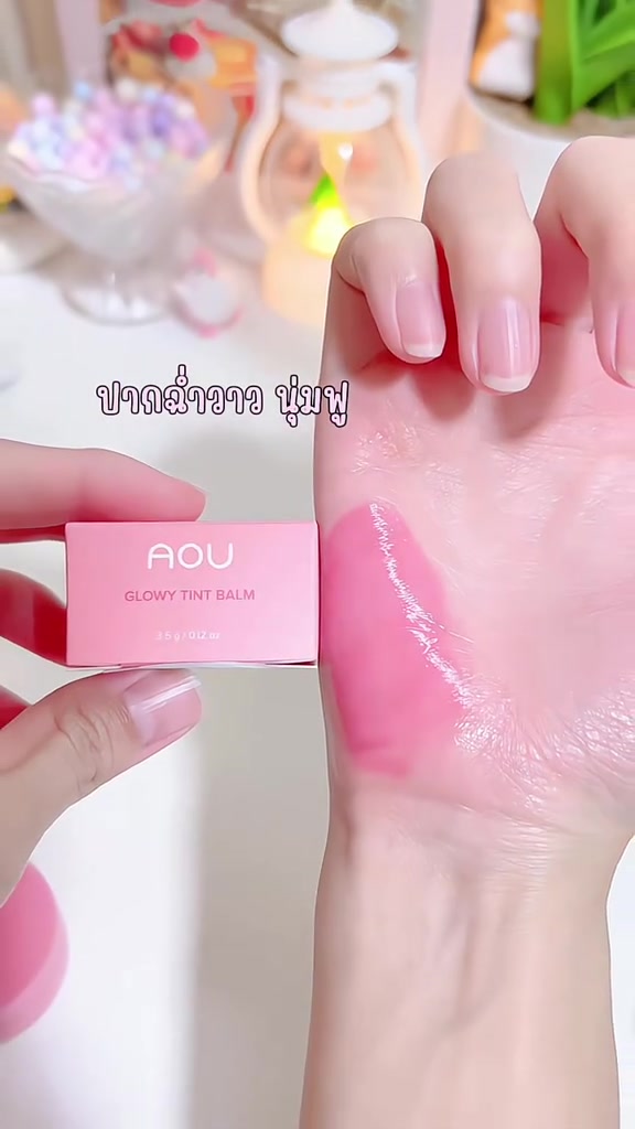 มือถือกล่องสีชมพูของเอโอยู โกลวี่ ทิ้นท์ บาล์ม ขนาด 3.5 กรัม คู่กับสวอชบาล์มสีชมพูเนื้อฉ่ำบนฝ่ามือ