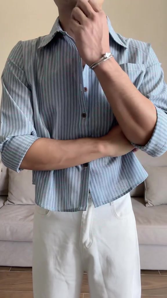 ลุคตัวอย่างเห็นตั้งแต่ช่วงคอลงมา เสื้อเชิ้ตลายทางพื้นฟ้าพับแขนใส่กับกางเกงขายาวสีขาว