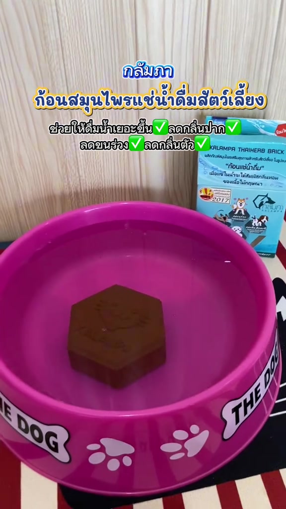 ก้อนสมุนไพรทรงหกเหลี่ยมสีน้ำตาลแช่ในน้ำภายในชามสีชมพู ข้างชามมีกล่องผลิตภัณฑ์สีฟ้า