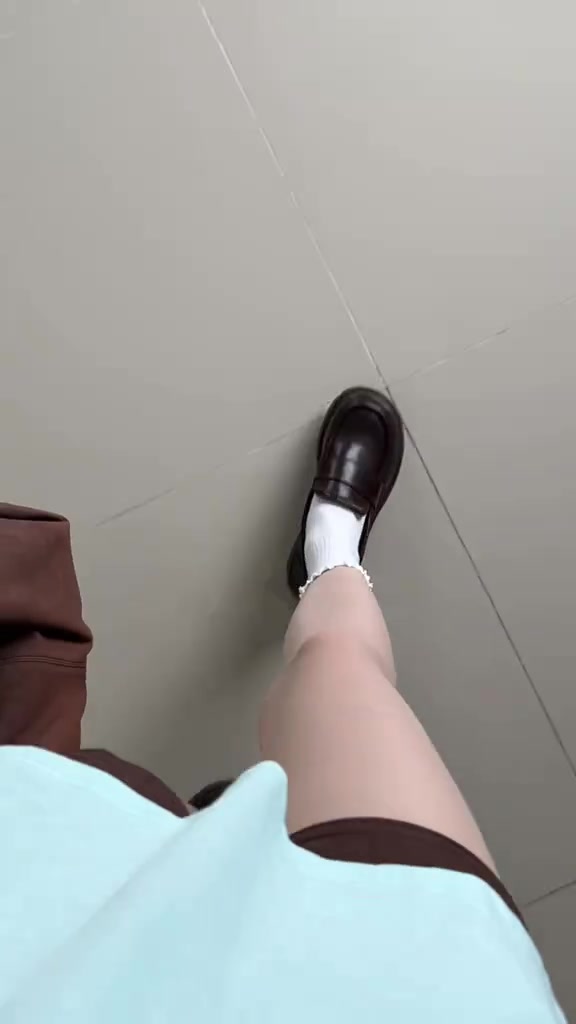 ภาพมุมมองระดับสายตาผู้ใส่ เห็นรองเท้าโลฟเฟอร์สีน้ำตาลเข้มหนึ่งข้างกับถุงเท้าขาวขณะก้าวเดินบนพื้นกระเบื้องสีเทา