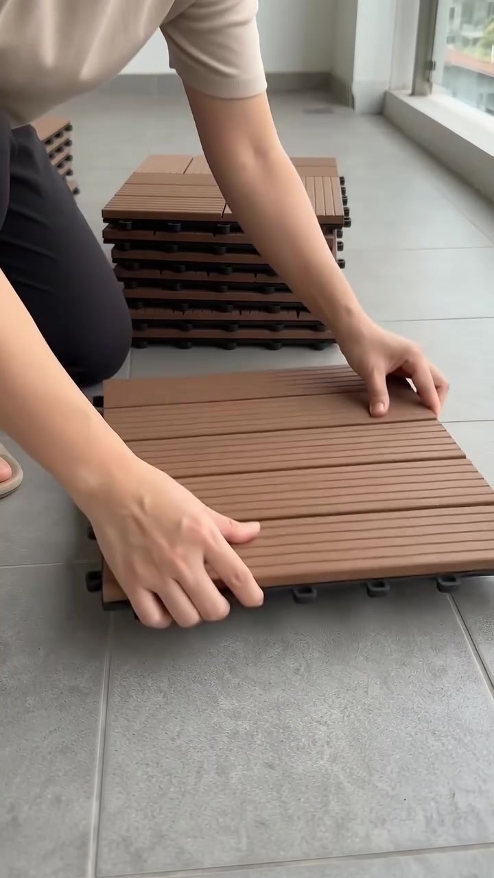 มือกำลังวางแผ่นปูพื้นลายไม้ต่อกันบนพื้นระเบียง