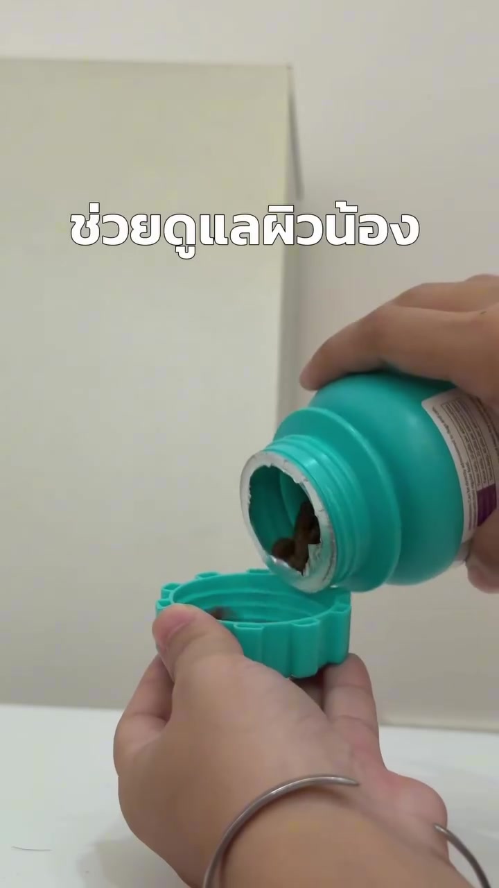 มือกำลังเปิดกระปุกเม็ดเคี้ยวเพ็ตฮีลเลอร์เหนือฝาสีเขียวอมฟ้า