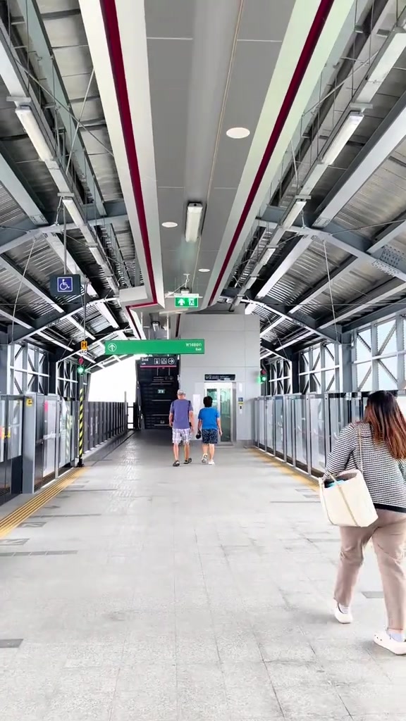 โถงทางเดินภายในสถานีรถไฟฟ้า มีป้ายบอกทางและผู้โดยสารเดินอยู่ด้านหน้า